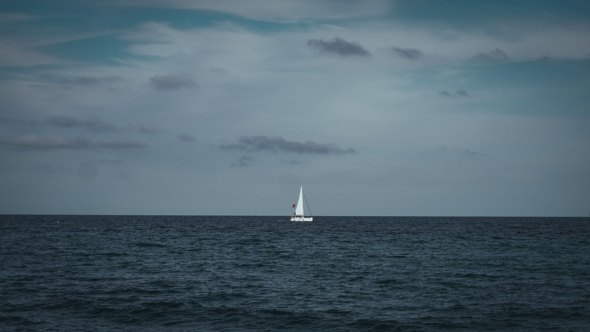 Samotna żaglówka na szerokim błękitnym oceanie pod chmurnym niebem